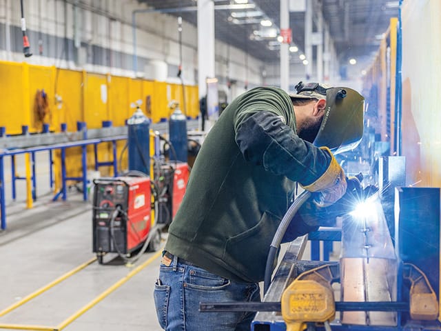 A welder wearing PPE working in a warehouse.