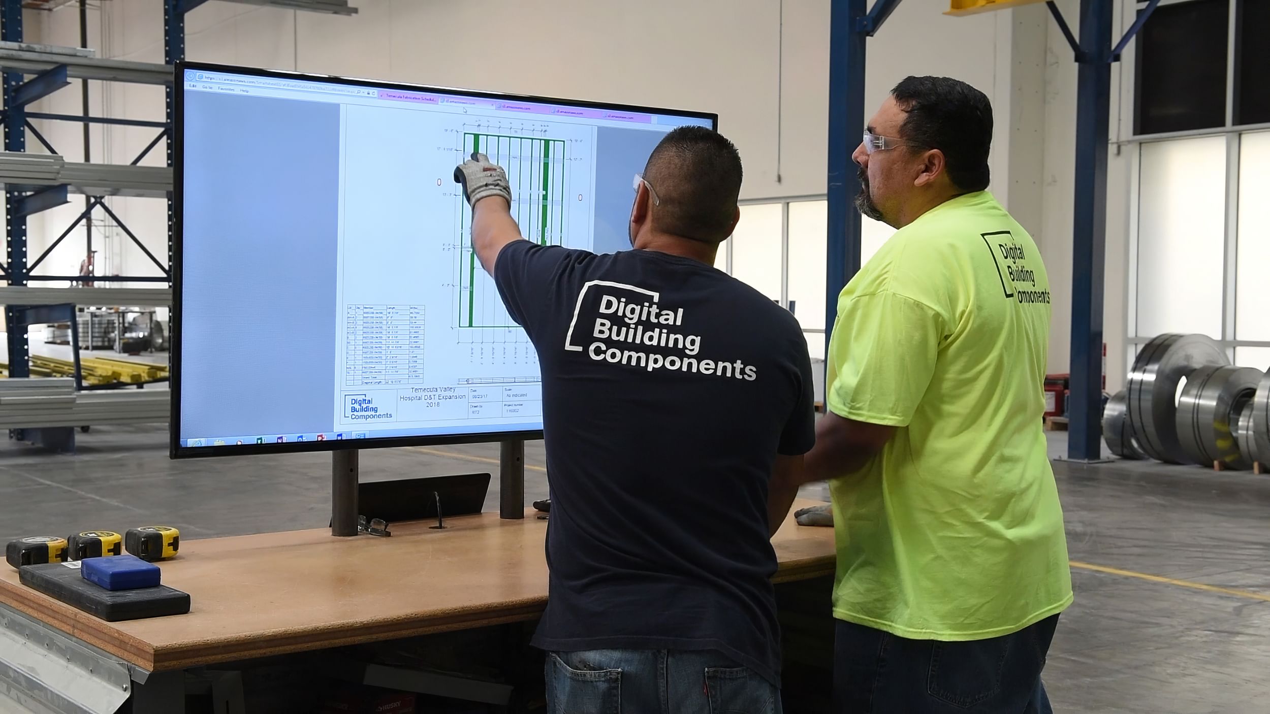 two workers discuss a screen in a factory