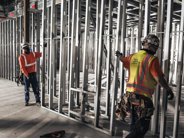 2 workers hold up prefabricated interior panel inside manufacturing facility