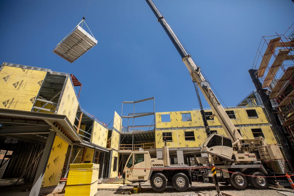 DBC prefabricated structural panel flying by crane into place above construction site