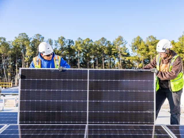 Two individuals wearing PPE holding a solar panel.