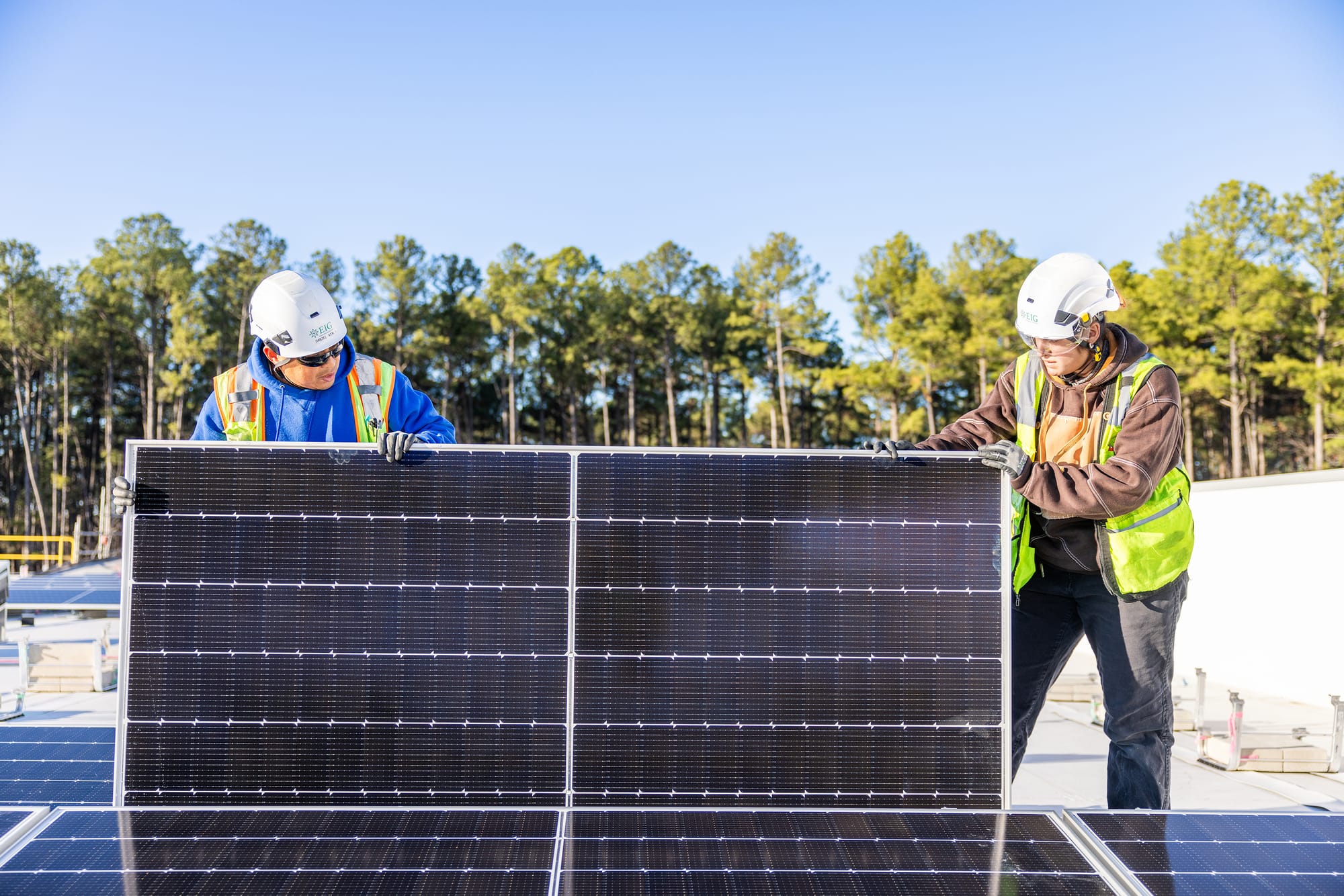 Two individuals wearing PPE holding a solar panel.