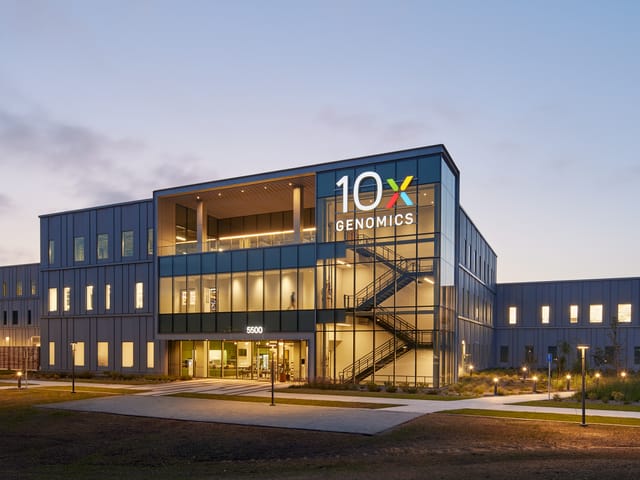 A sunset picture of a three story building with glass hallways. The signage reads "10X Genomics"