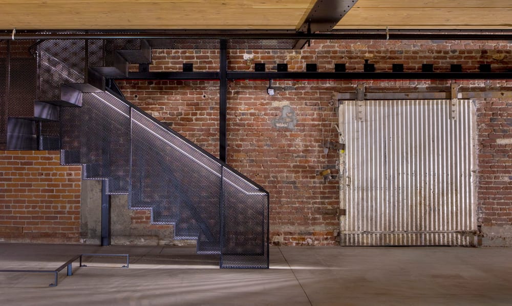 A brick wall with a staircase to the left, there is also a metal panel door