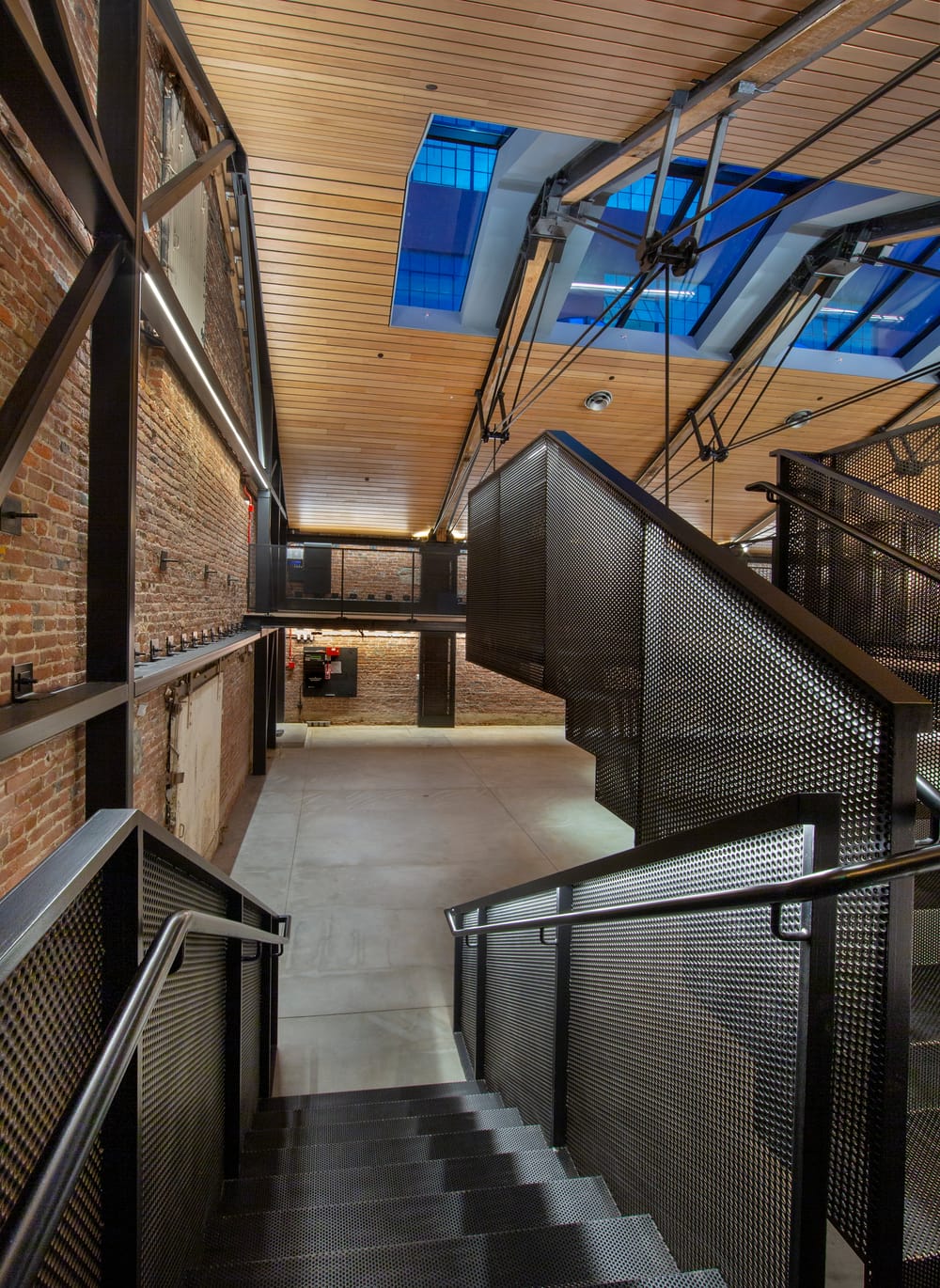 The inside of a building that has a wooden roof, exposed brick walls and a black steel staircase that is lit up.