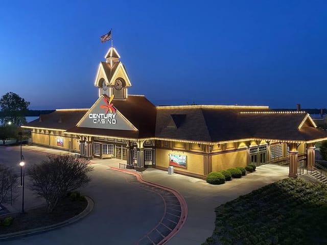 Night view of a one story building with a clock tower at the entrance, big sign at the front that reads "Century Casino". The building is outlined with lights