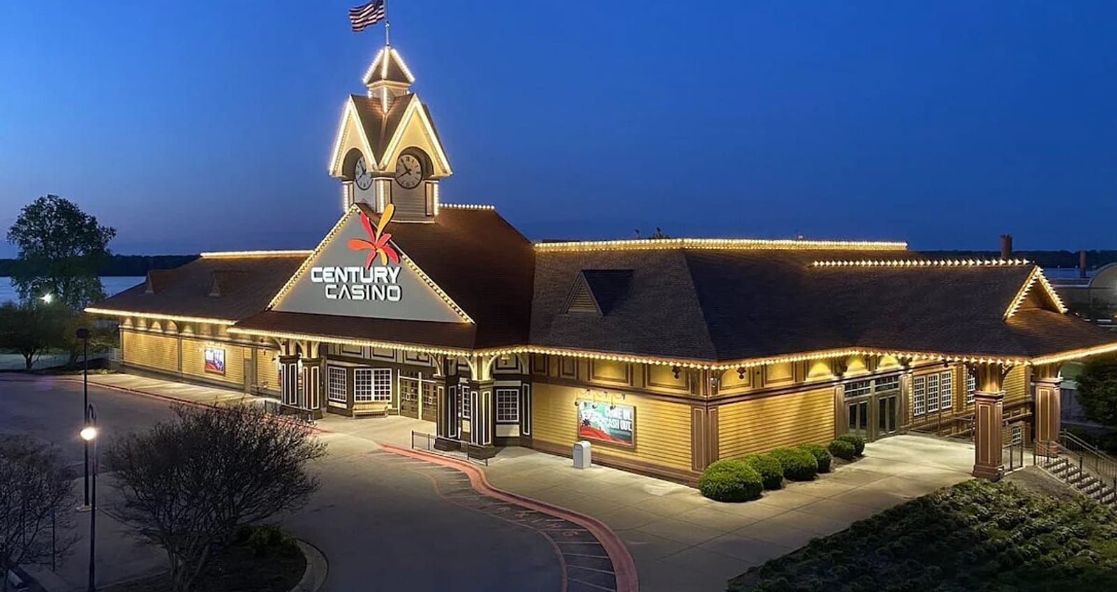 Night view of a one story building with a clock tower at the entrance, big sign at the front that reads "Century Casino". The building is outlined with lights