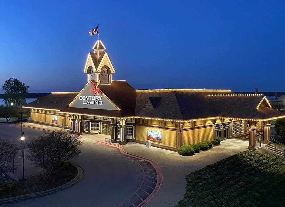 Night view of a one story building with a clock tower at the entrance, big sign at the front that reads "Century Casino". The building is outlined with lights