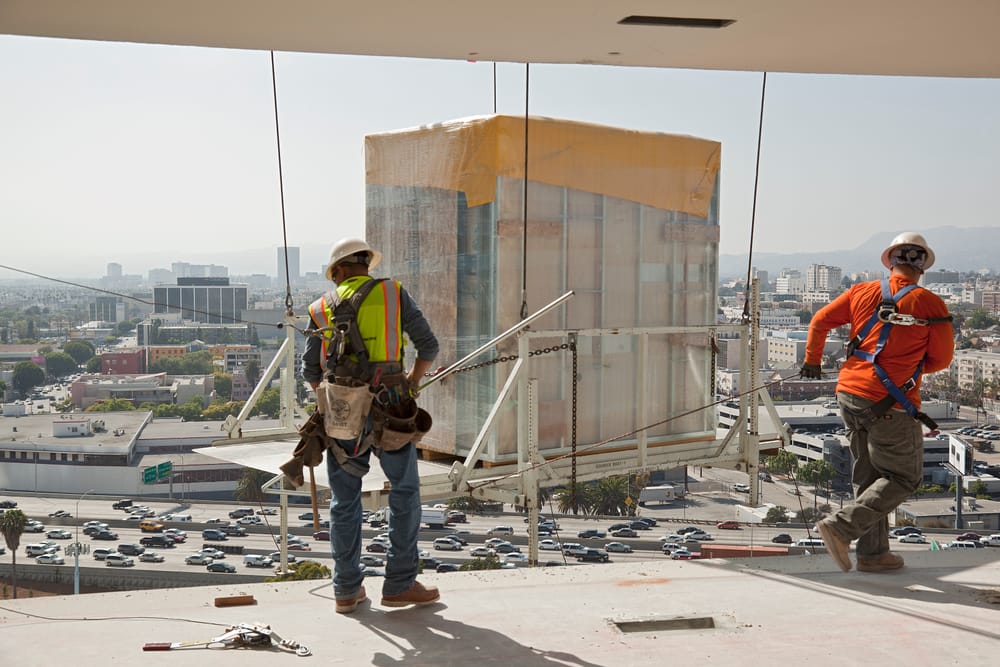Two construction men pulling and installing bathroom pod flying in