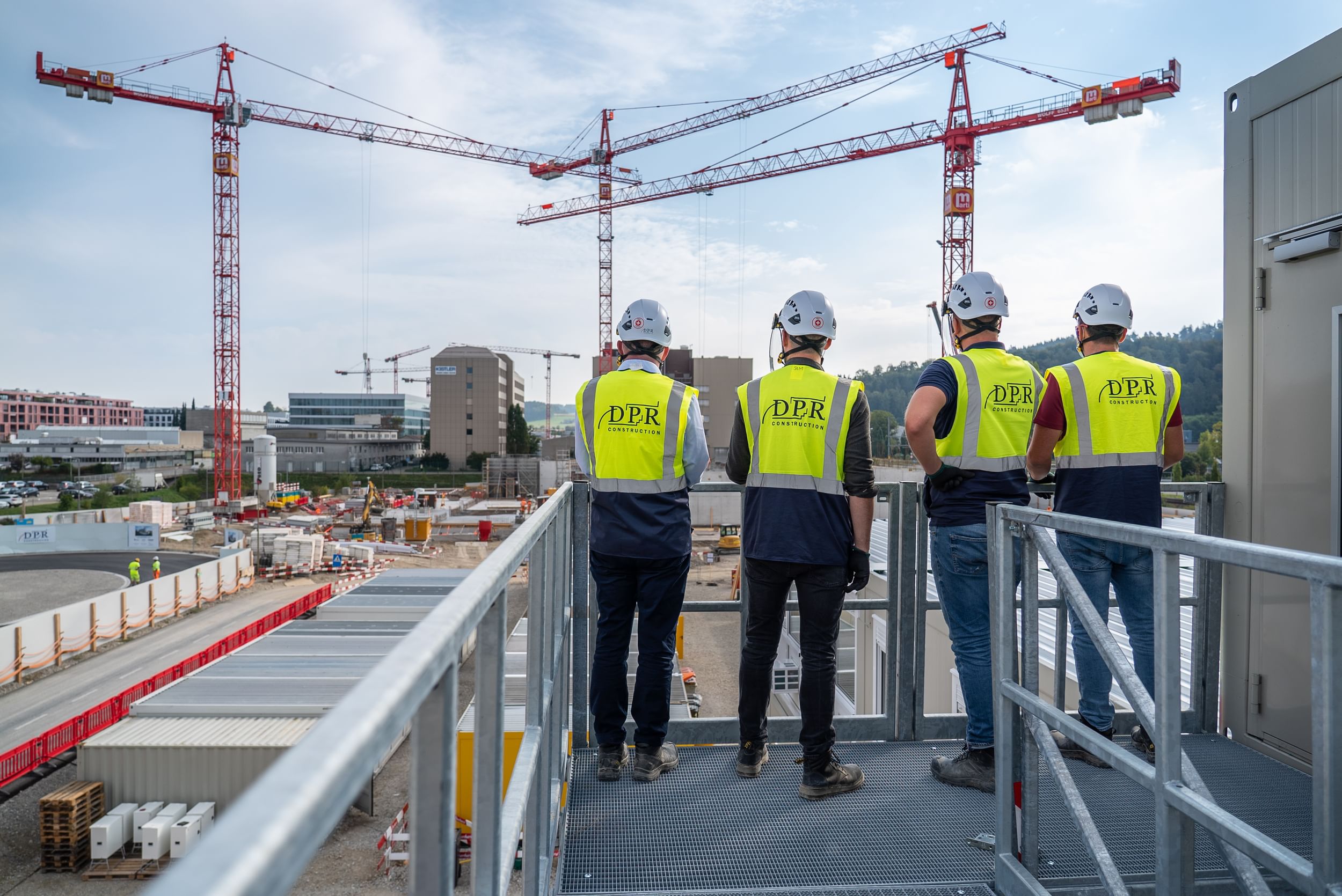 Four people in DPR Construction vests survey a large project.